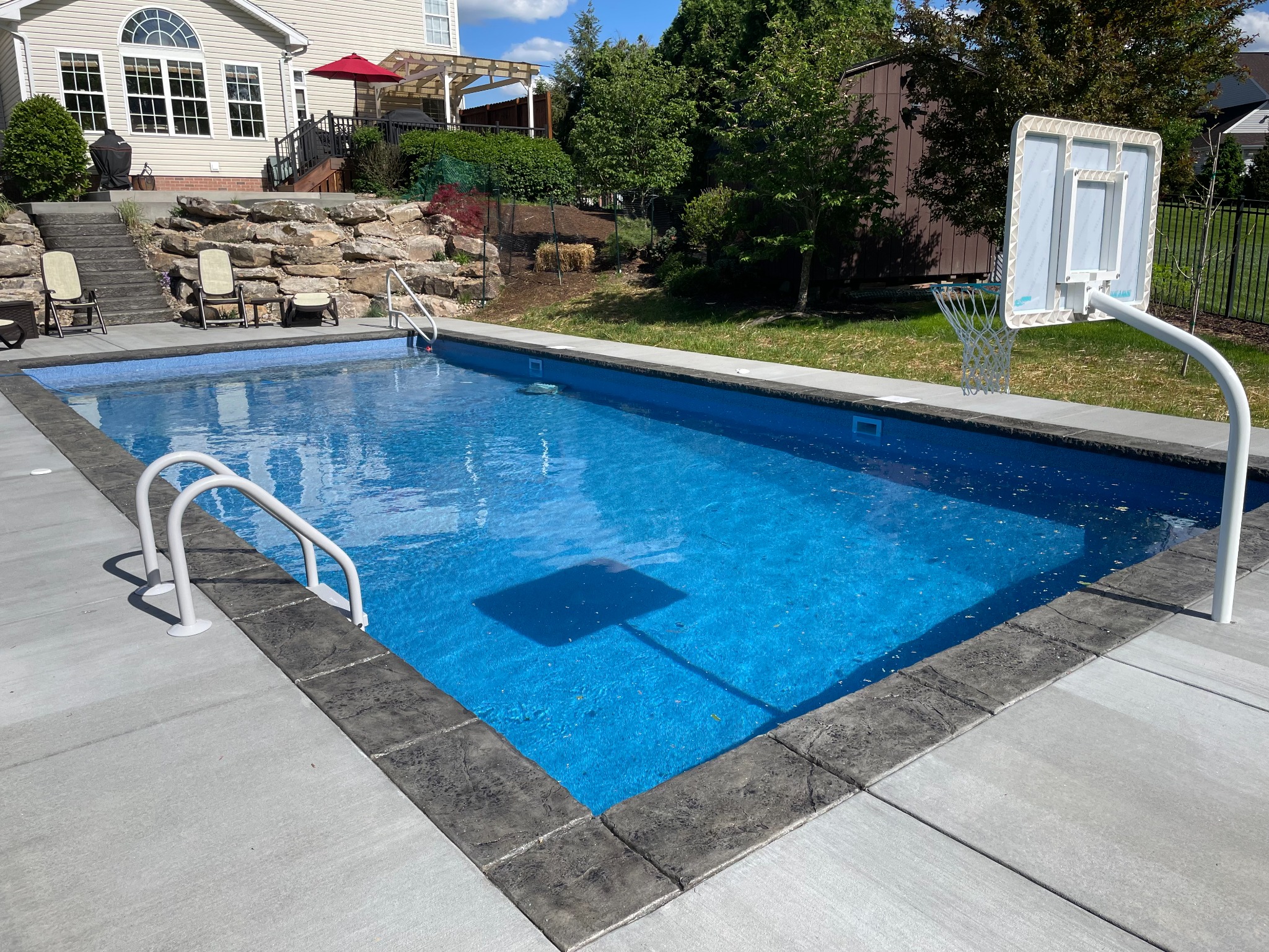 Rectangular pool with basketball setup and wide concrete deck